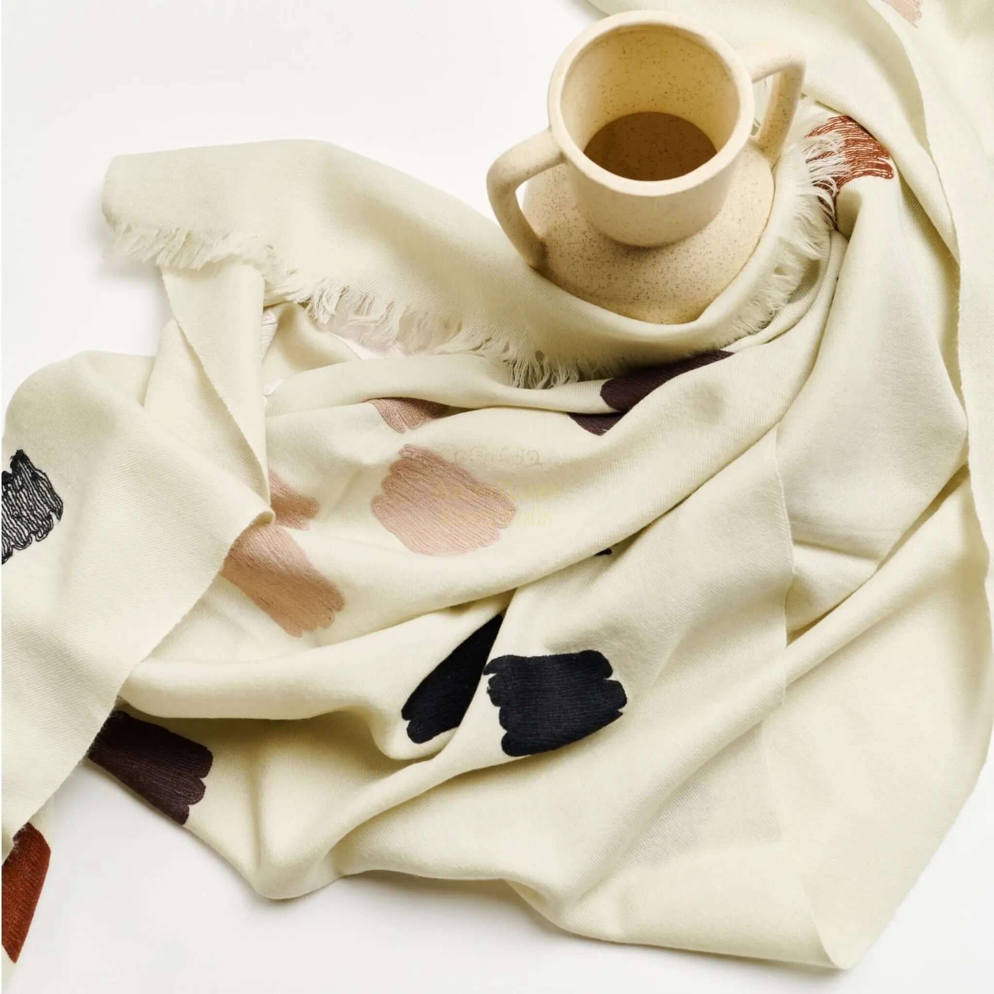 Hand woven embroidered scarf displayed with a ceramic mug, featuring artistic brushstroke patterns in soft colors.