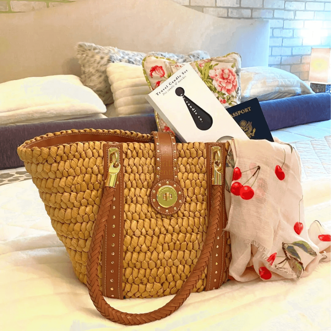 Coastal travel scented candles set alongside a stylish woven bag, travel essentials including a passport and scarf.