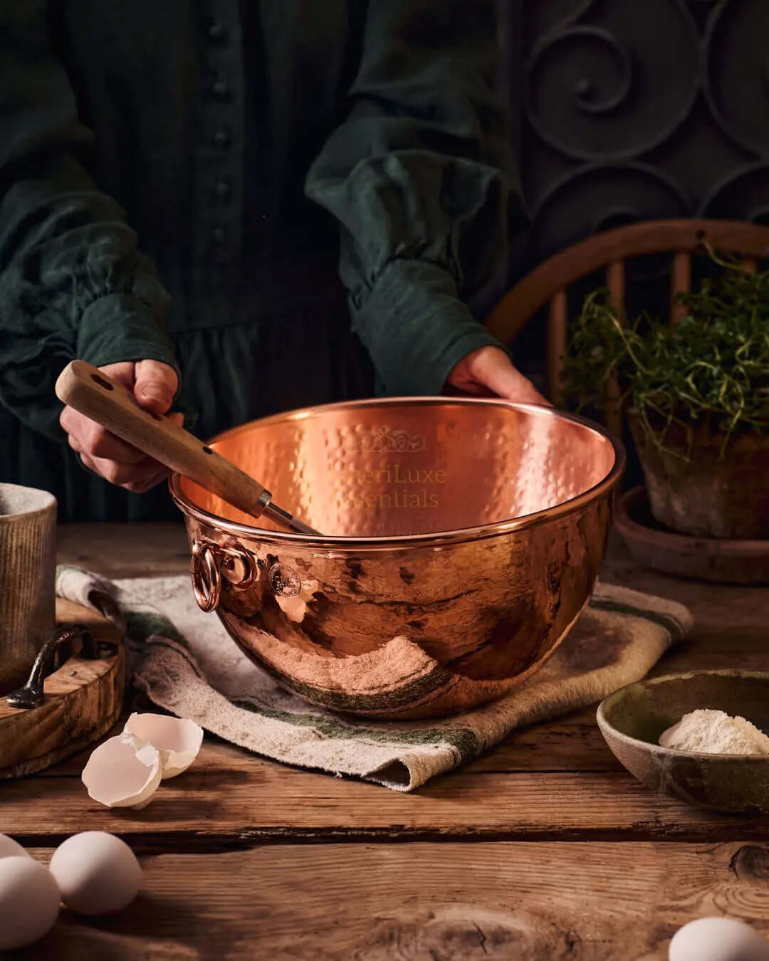 Hands holding a CMK farmhouse kitchen copper mixing bowl with a wooden spoon, showcasing its rustic charm and elegant finish.