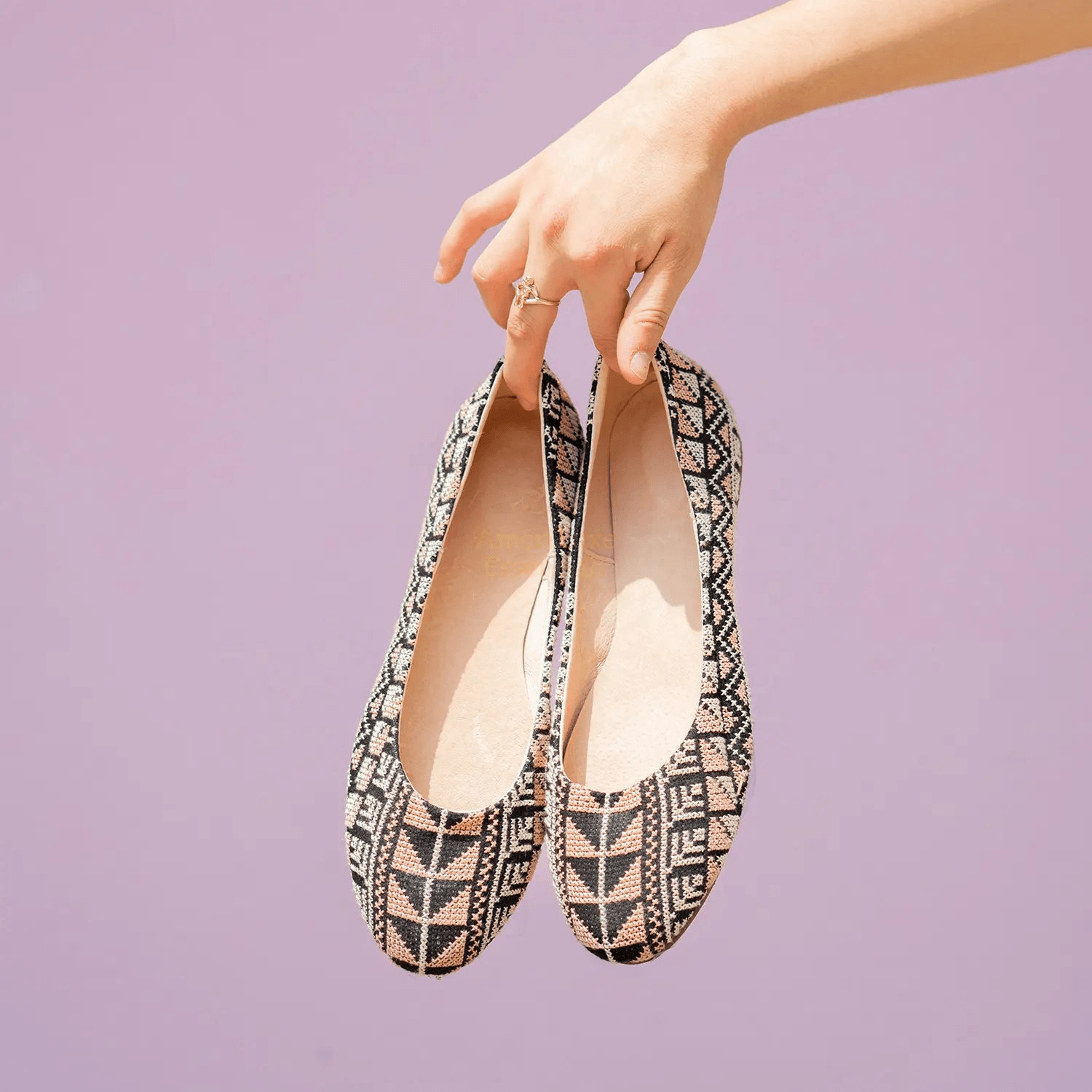 Hand holding Yasmin rose pink comfortable flat shoes with tatreez design against a purple background.