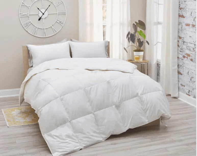 Luxurious white down comforter on a bed with two pillows and decorative clock in a bright room.