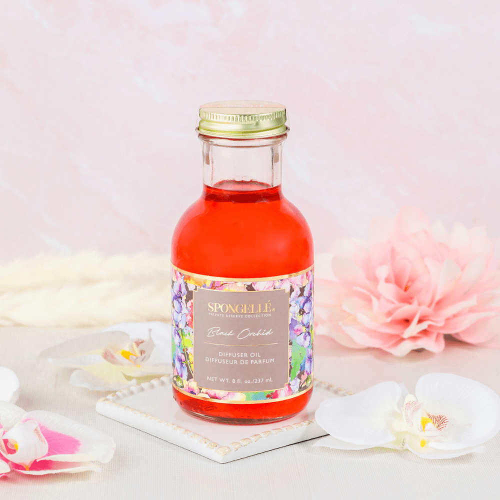 Black Orchid Diffuser Oil | Private Reserve Collection in a glass bottle with colorful flowers in the background.