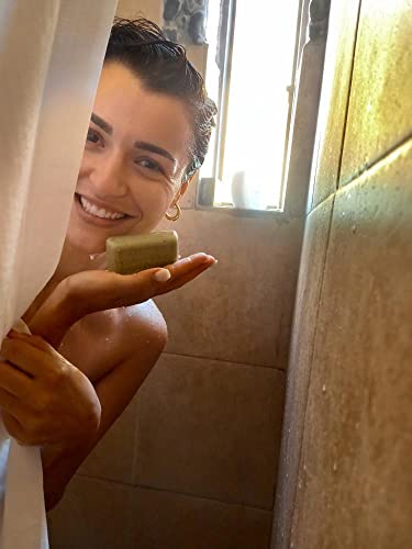 Woman smiling in the shower holding natural olive oil soap three pack, showcasing its use in skincare.