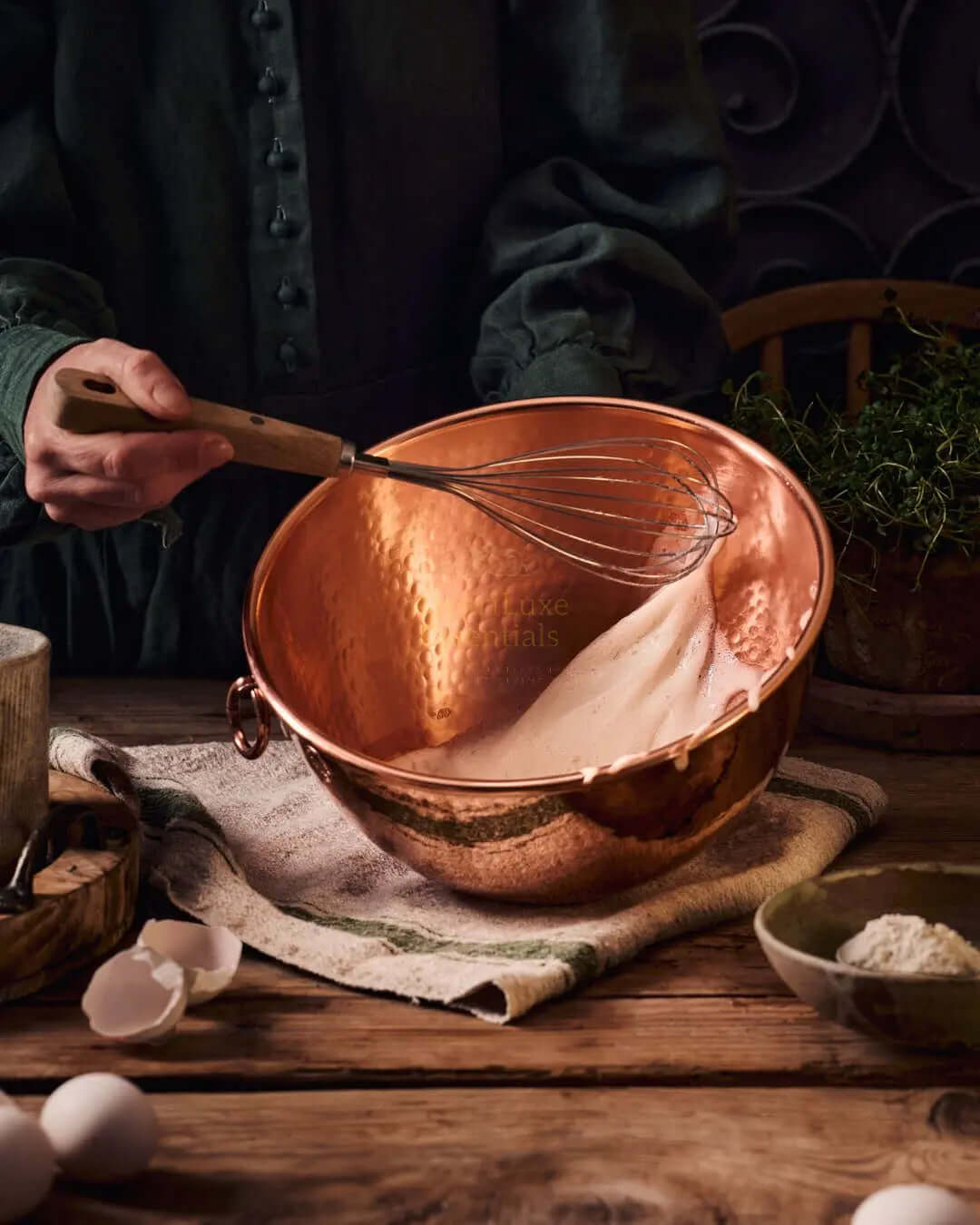 Person using a farmhouse kitchen copper mixing bowl with flour and a whisk on a rustic wooden table.