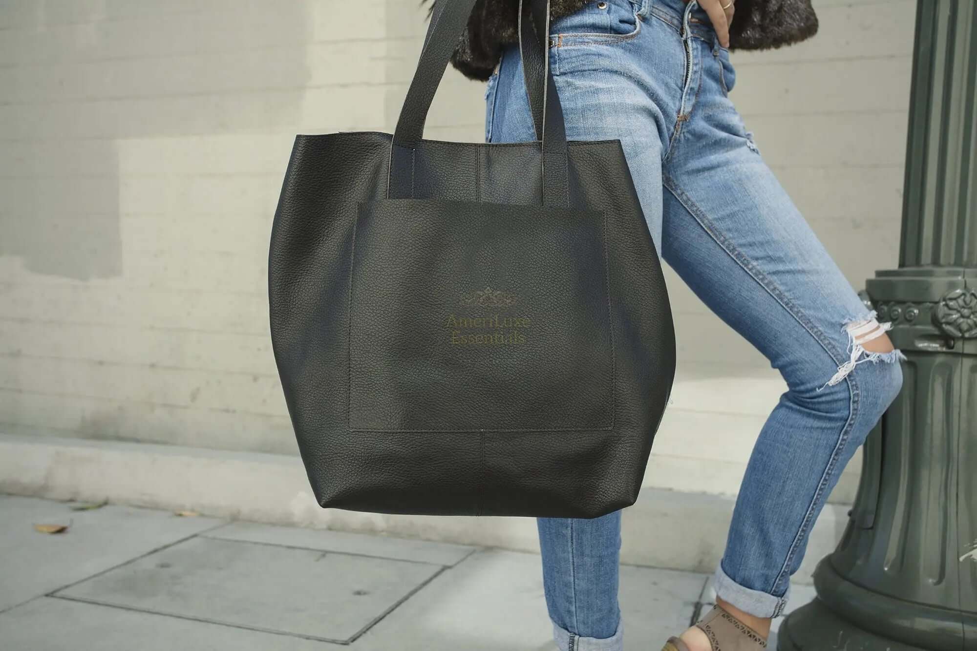 Professional journalist tote bag in black, held by a person wearing jeans, showcasing its sleek design and spacious interior.
