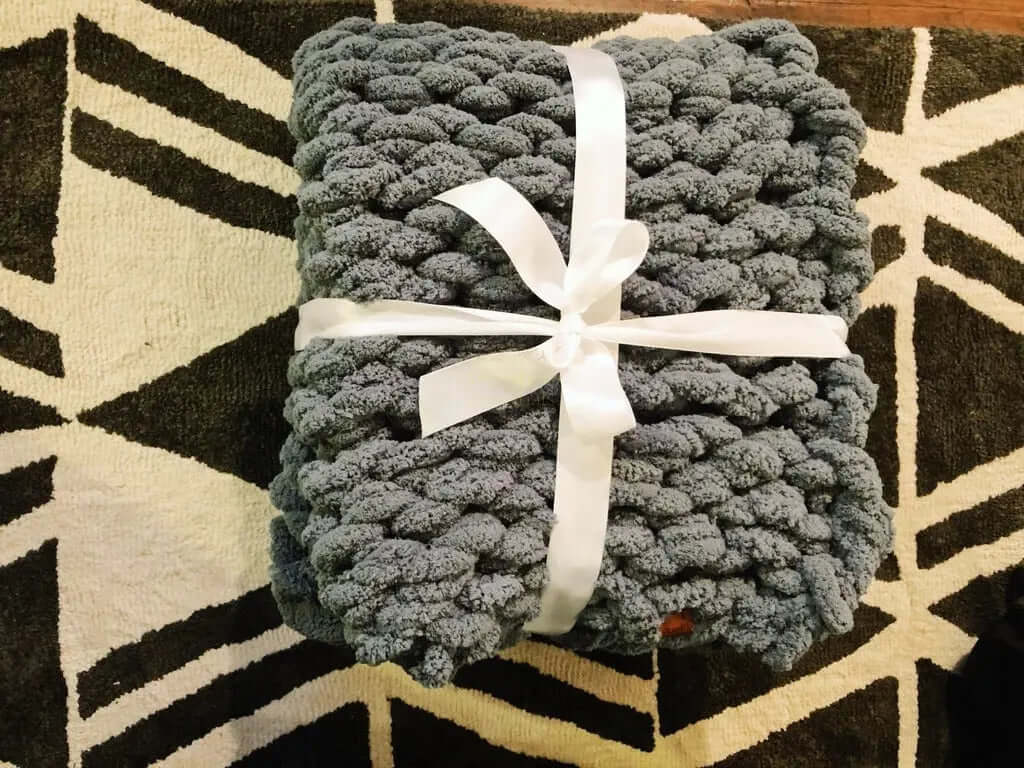 Dark gray chunky knit blanket tied with a ribbon on a stylish rug.