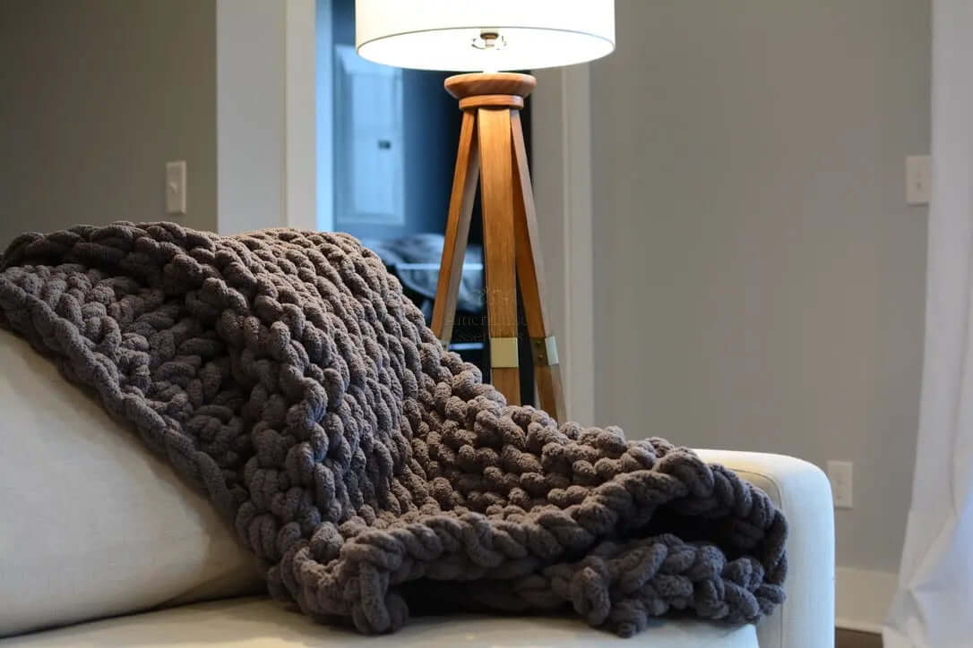 Cozy dark gray chunky knit blanket draped over a couch next to a stylish lamp.