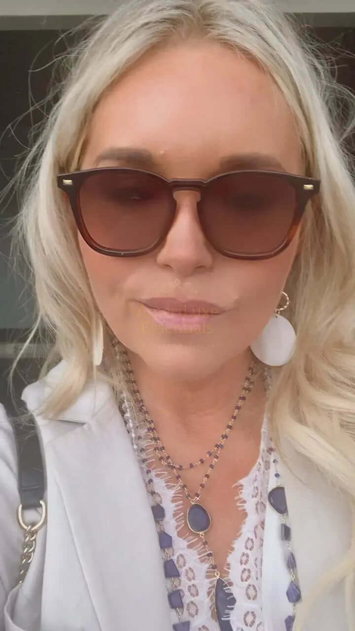 A person wearing sunglasses and a white outfit, showcasing a double sapphire necklace with sapphire drop accessories.