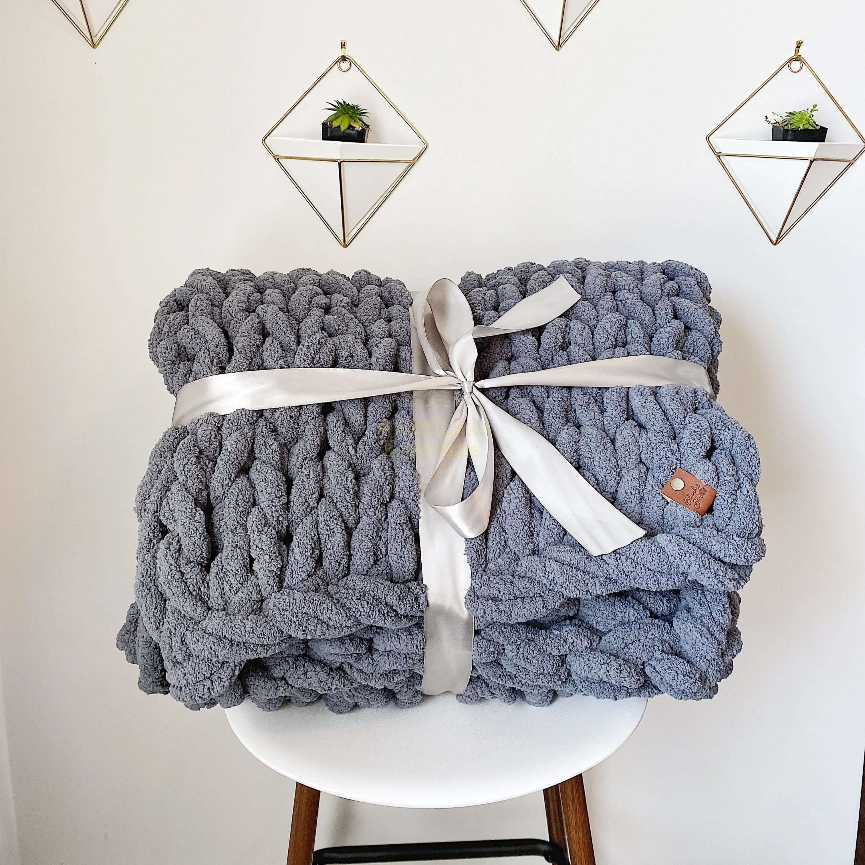 Dark gray chunky knit blanket elegantly tied with a ribbon, displayed on a chair.