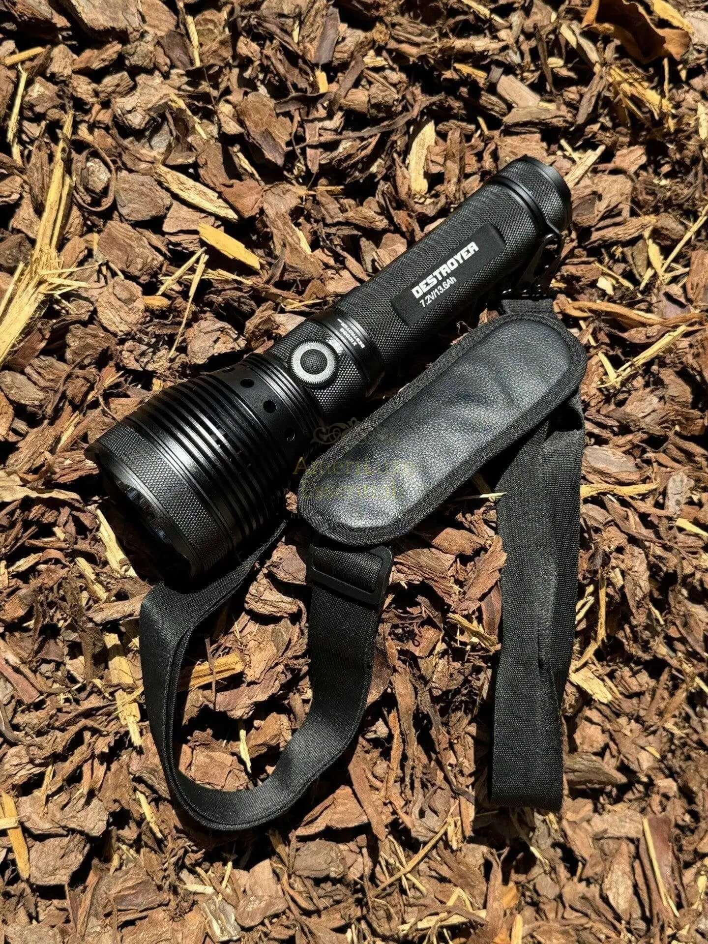 9500 lumen search light resting on a bed of mulch with a strap attached.